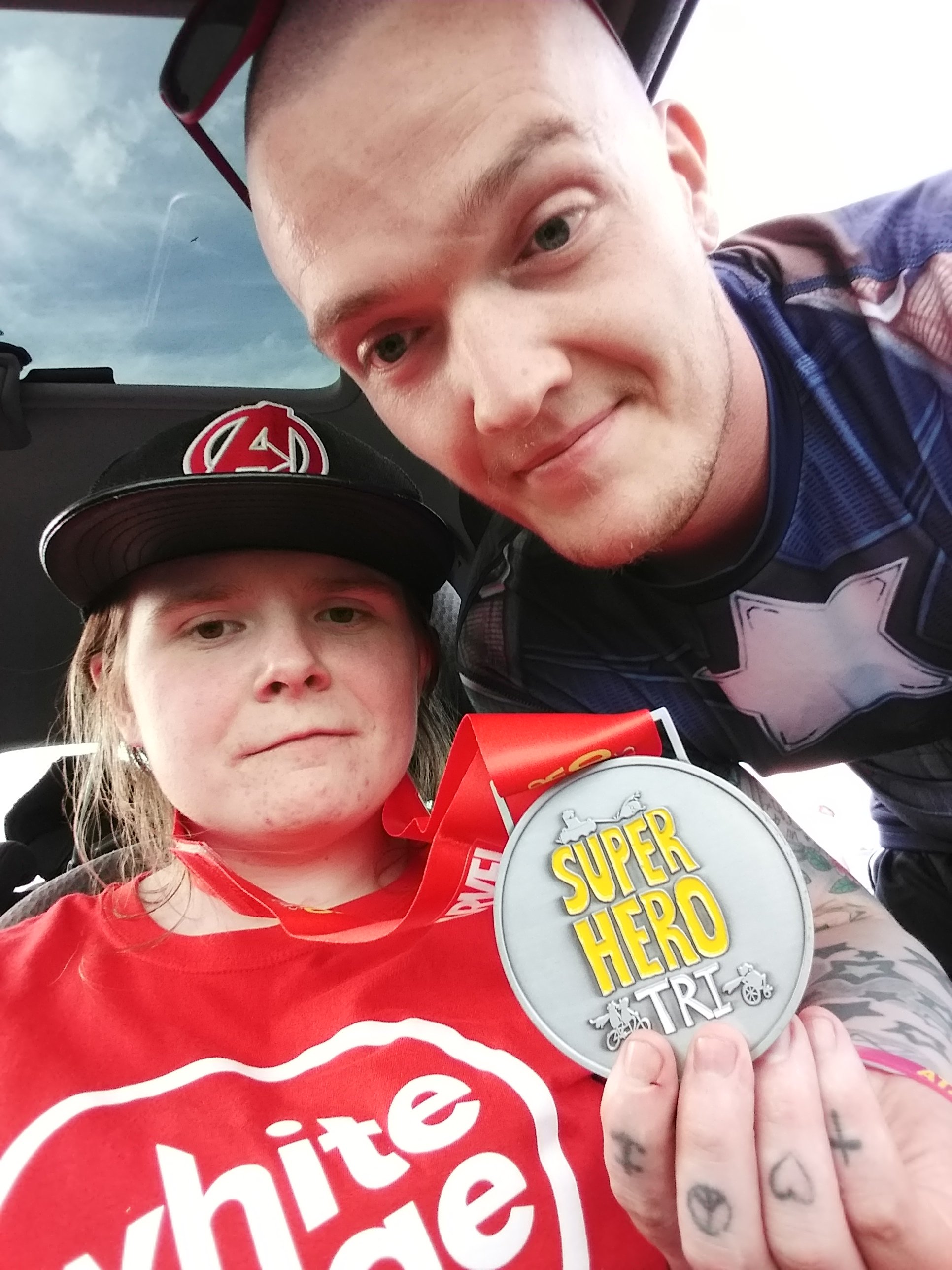 Ami has just transferred into the car after leaving the Superhero Tri. Ewan is beside her, holding up a medal. They look shattered.