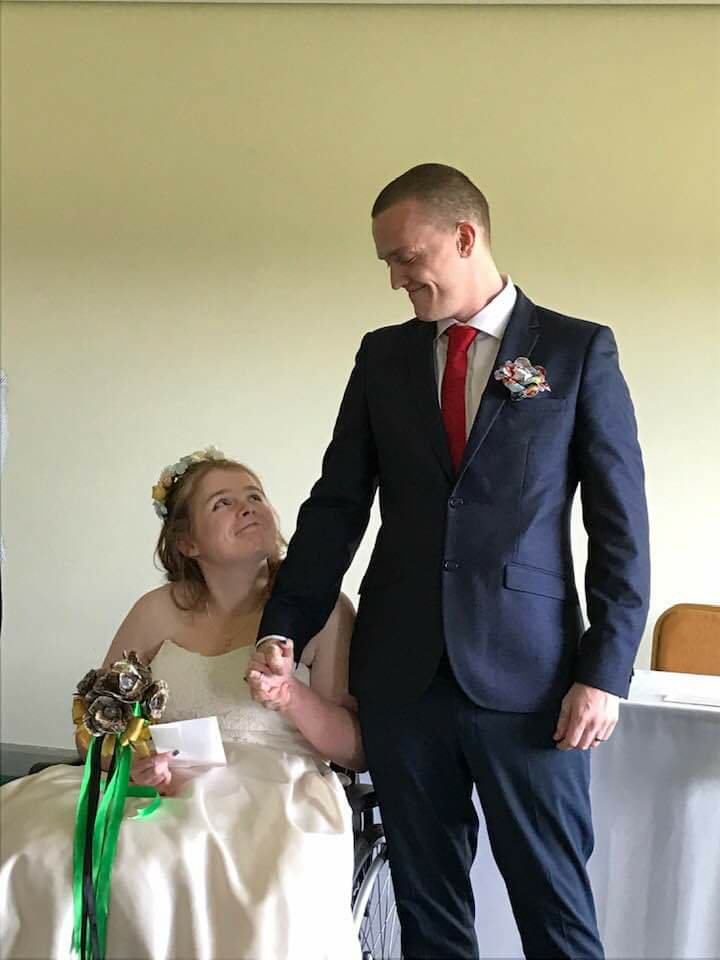 Ami and Ewan are looking at each other and smiling. They have just got married