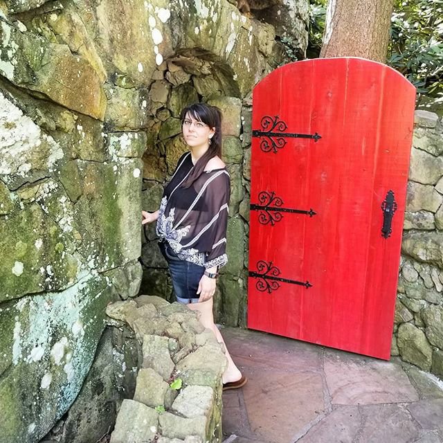 Savannah is standing under an old archway with a big red door opened