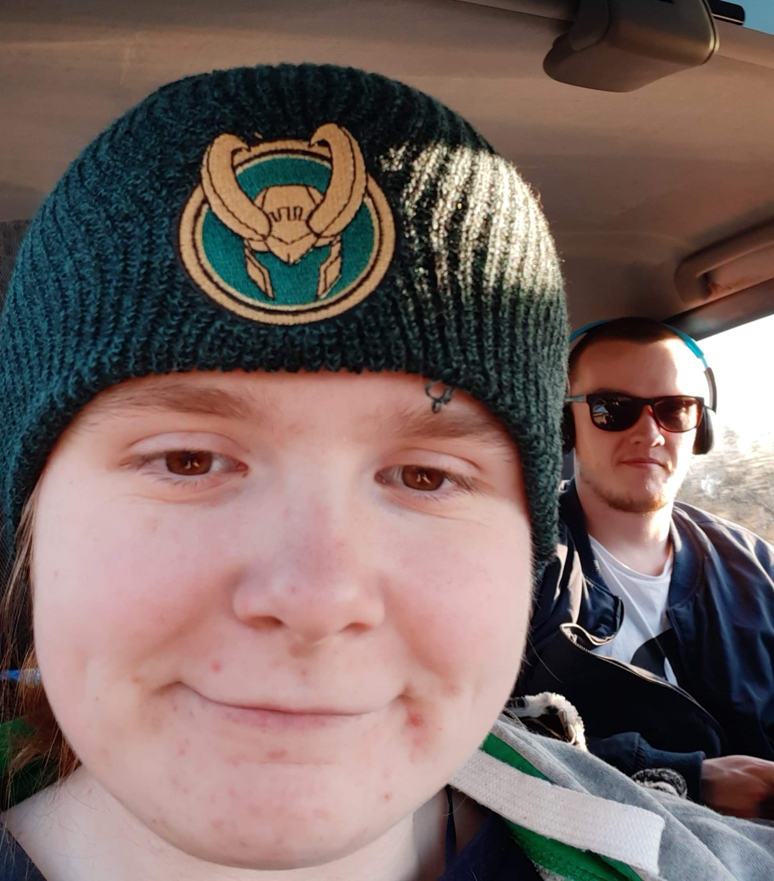 Ami and Ewan are in the car. Ami is wearing her new Loki beanie, which is dark green and has a Loki helmet symbol on the front