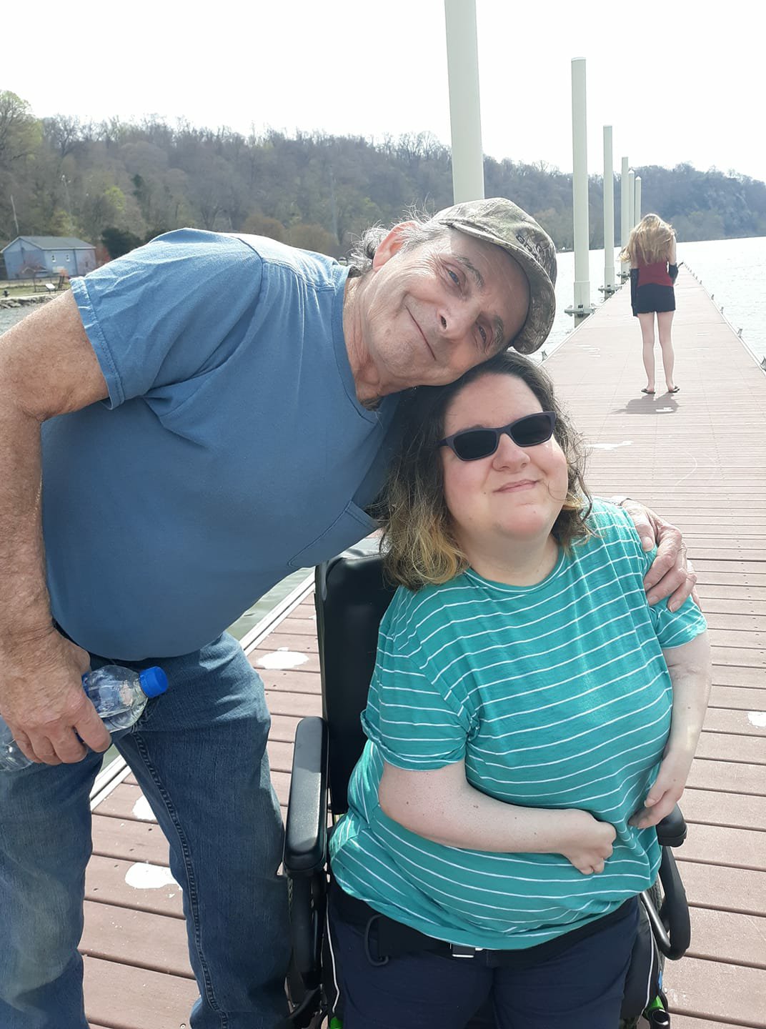 Nikole and her Dad are smiling at the camera. They are on a pier with water stretched in the background.