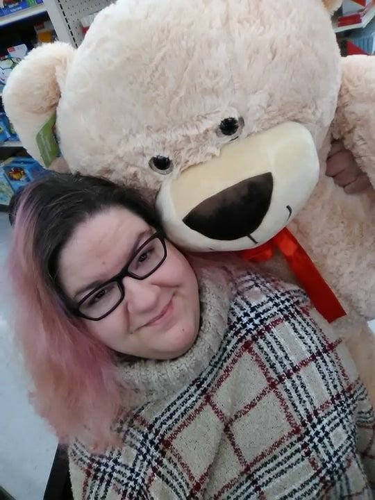 Nikole is smiling and holding a very large cuddly bear with a red bow.
