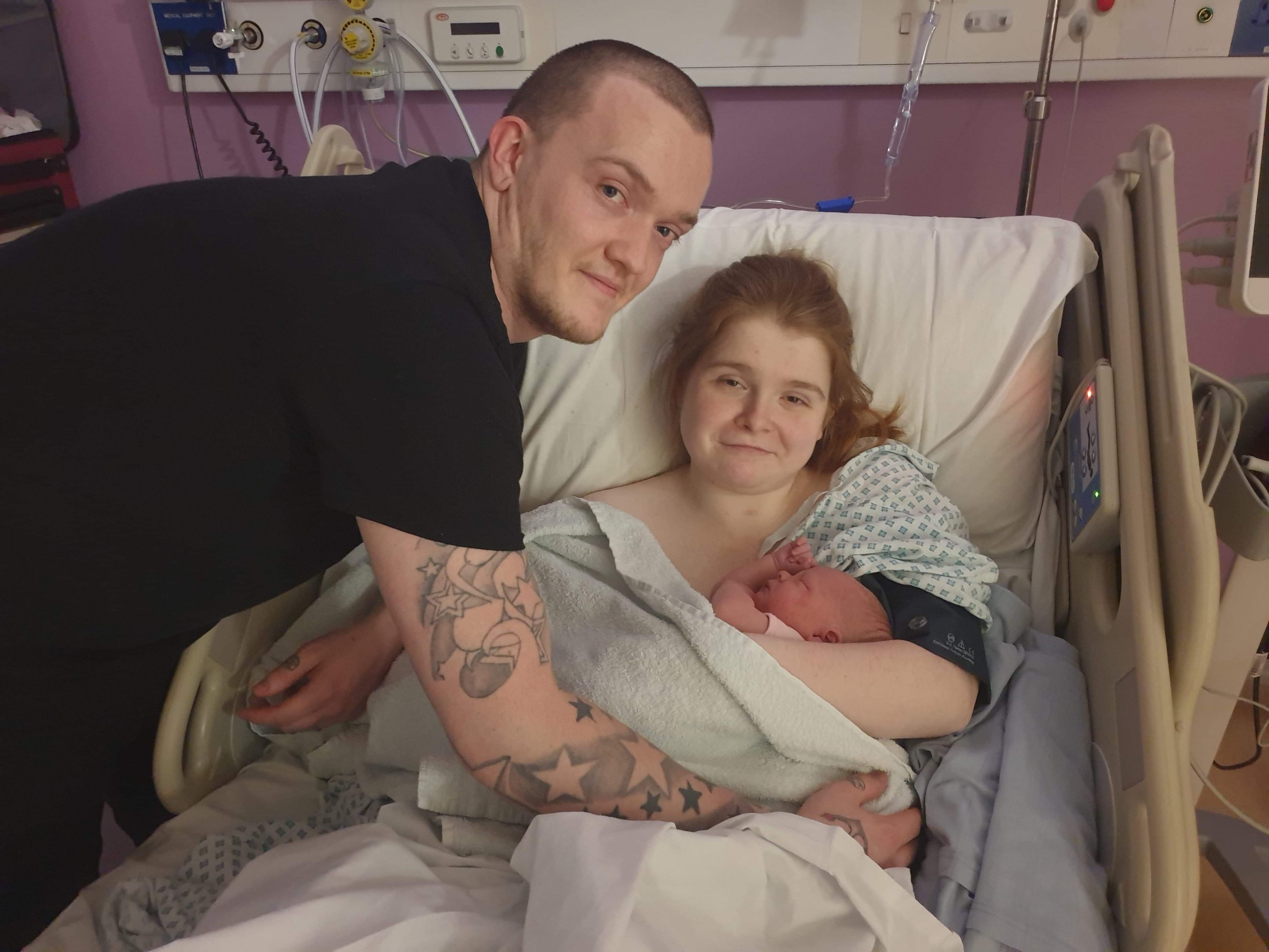 Photo of Ewan, Ami and Daisy. Ewan and Ami are smiling while cradling Daisy