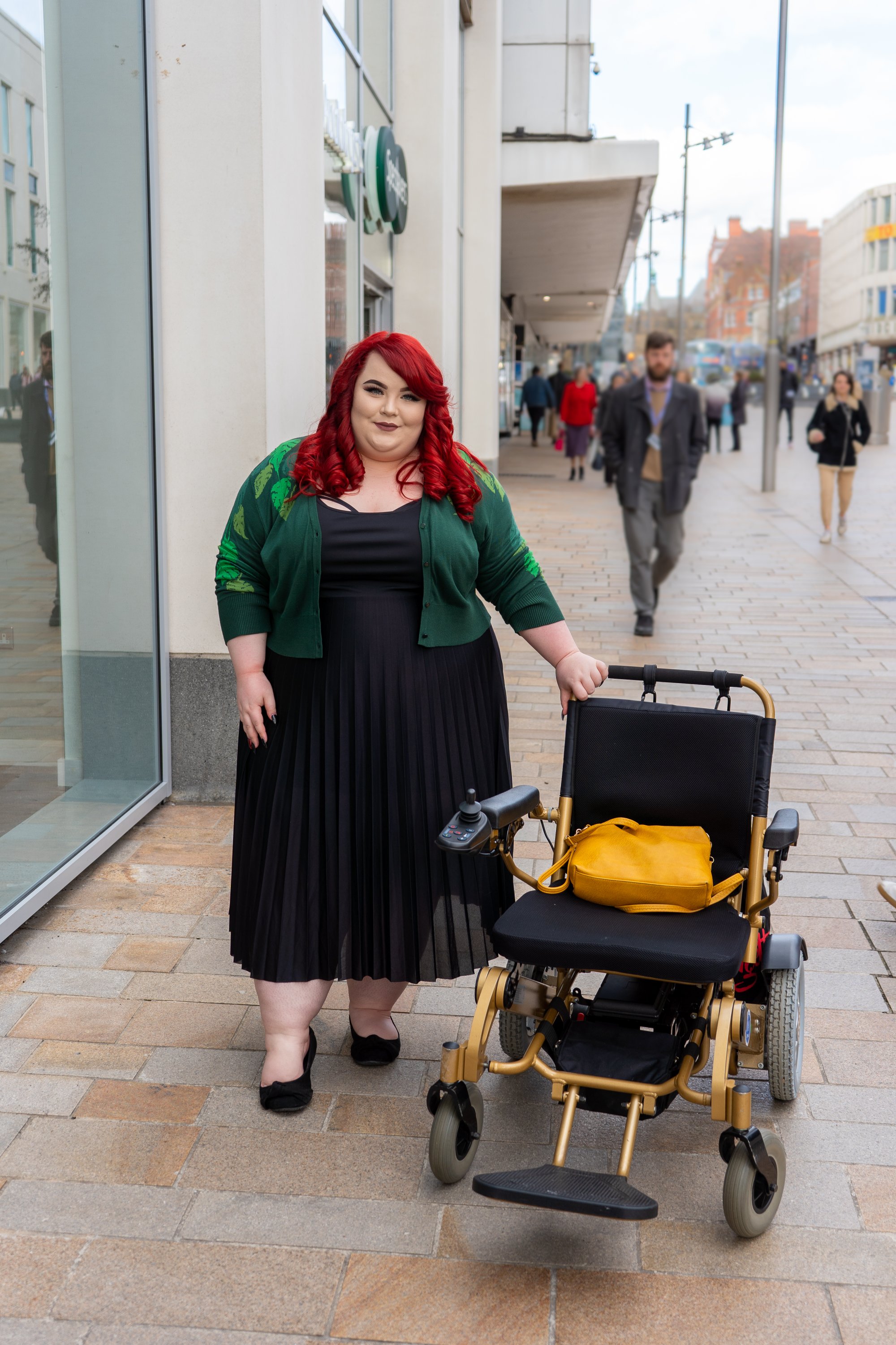Photo of Georgina standing next to her powerchair.