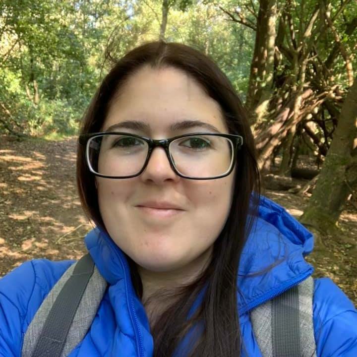 Mel is smiling at the camera, she is surrounded by trees in the woods/a forest