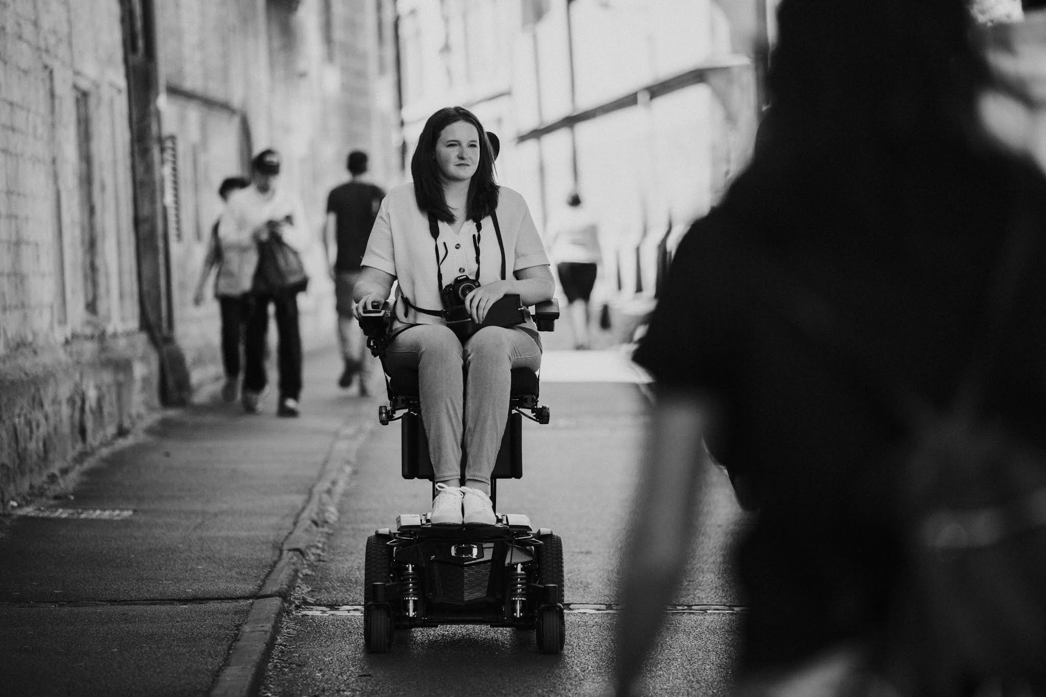 A black and white photo of Shona, in her powerchair with her camera, looking into the distance.
