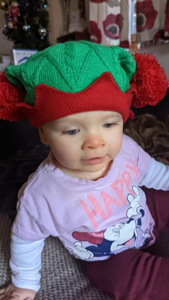 Daisy is wearing a knitted elf hat, with very big red bobbles at each side