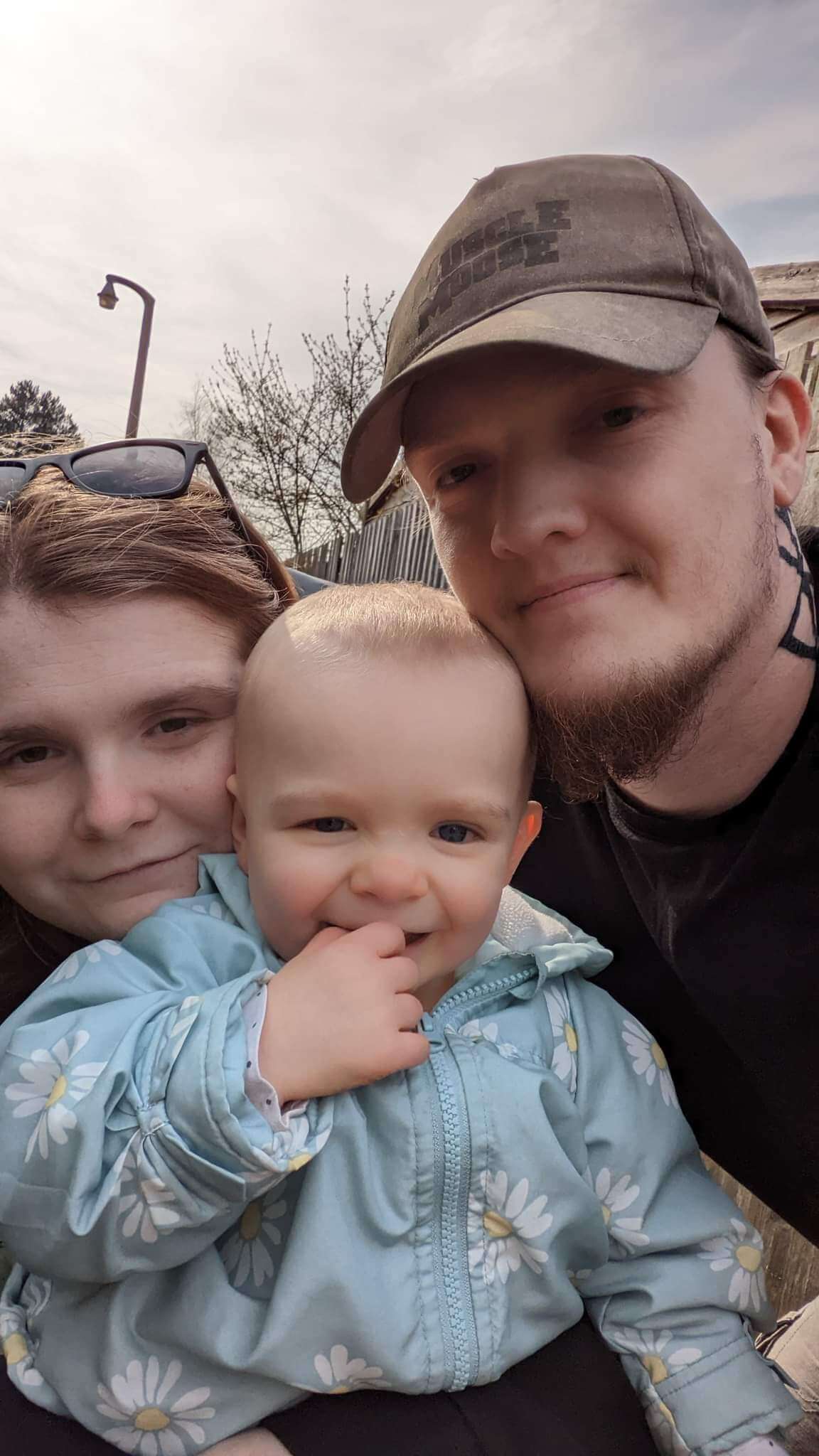 Ami, Daisy and Ewan are huddled close together, smiling at the camera.